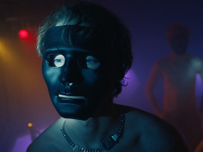 A young man wears a black mask in a nightclub.