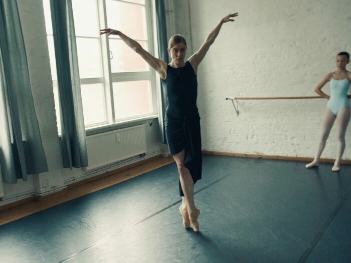 A ballet instructor demonstrates a move, observed by her student.