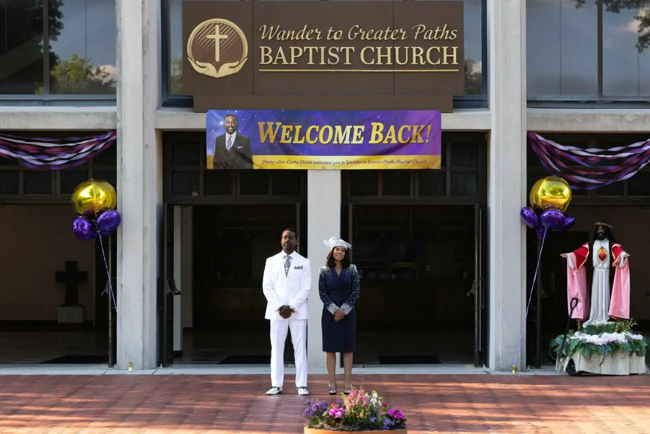 A husband and wife pair stand in front of a large church entrances