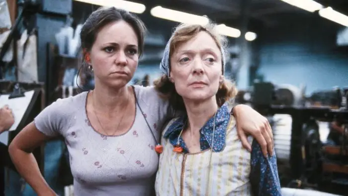 Two women stare glumly in a factory.