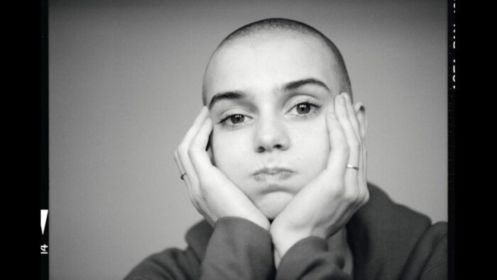 Sinéad O'Connor stares at the camera with hands on cheeks in NOTHING COMPARES. 