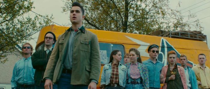 A young man and several companions in front of a school bus.