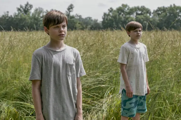 Two young twin boys stand in a field.