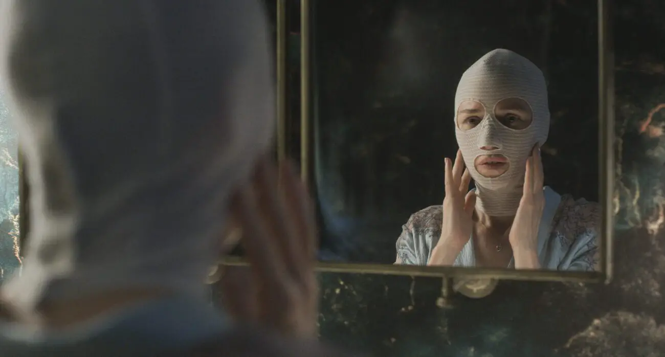 A woman in a white post-surgery mask looks at herself in a mirror