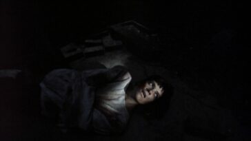 A woman lies on her back in a straightjacket with light across her face