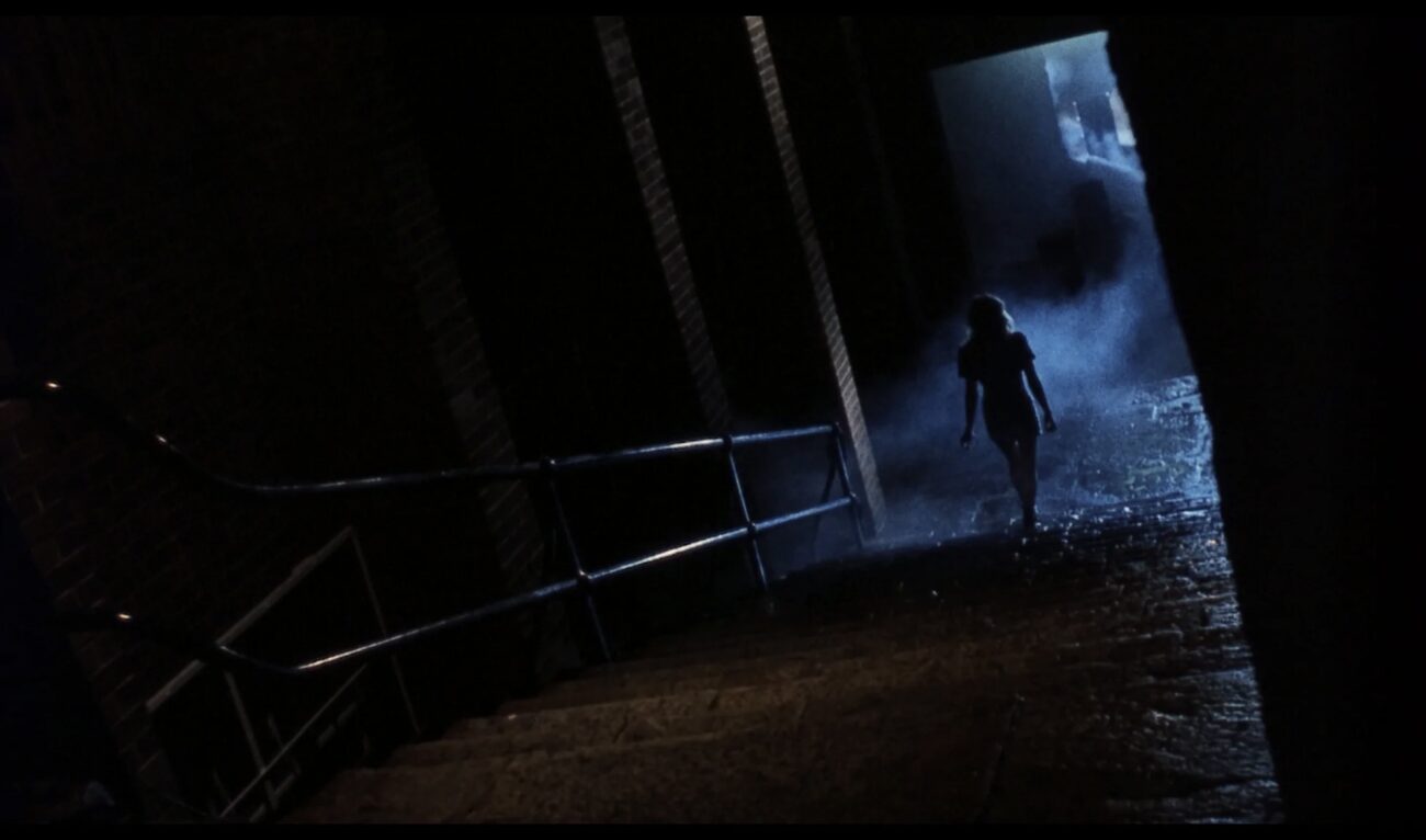 A woman walks up darkened stairs.