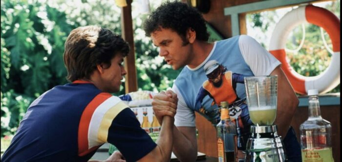 Dirk (Wahlberg) and Reed (Reilly, dressed in colorful '70s t shirts, clasp hands at Jack's pool party.