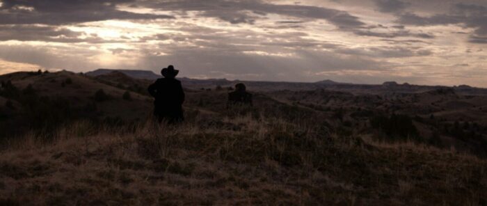 Two cowboys face off in the Badlands at sunset.
