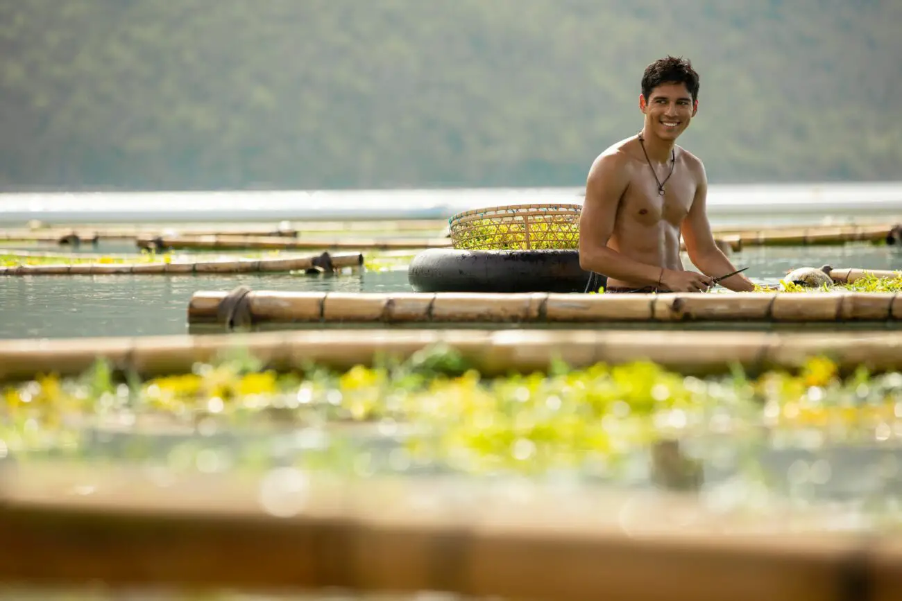 A shirtless seaweed farmer looks over with a smile in Ticket to Paradise