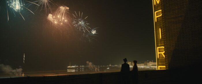 Two people watch fireworks from the roof of a theater.