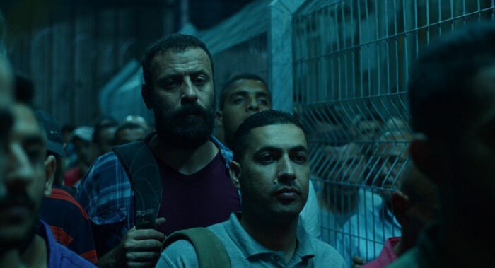 Ali Suliman (center, middleground) as Mustafa stands in line for his work permit in 200 Meters.