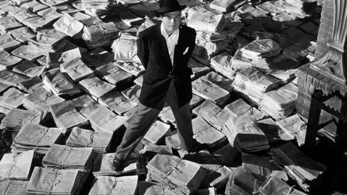 Orson Welles as Charles Foster Kane stands above stacks of newspapers in Citizen Kane.