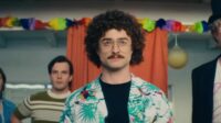 Daniel Radcliffe as "Weird Al" Yankovic at the pool party with his accordian, his bandmates behind him and Rainn Wilson as Dr. Demento to his right