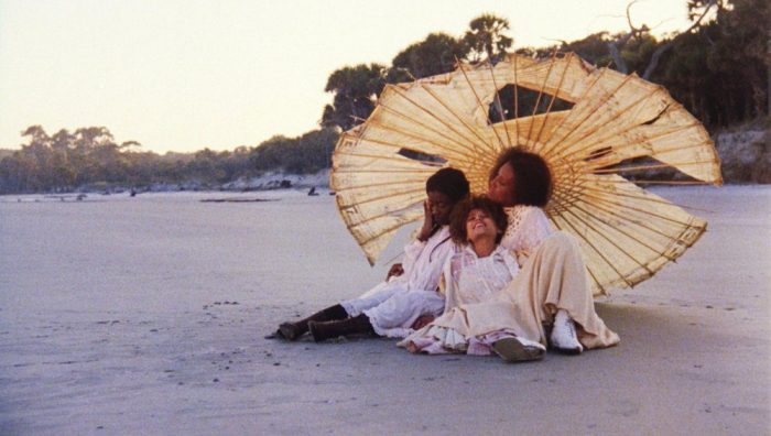 A woman and two children sit beneath a parasol on a beach.