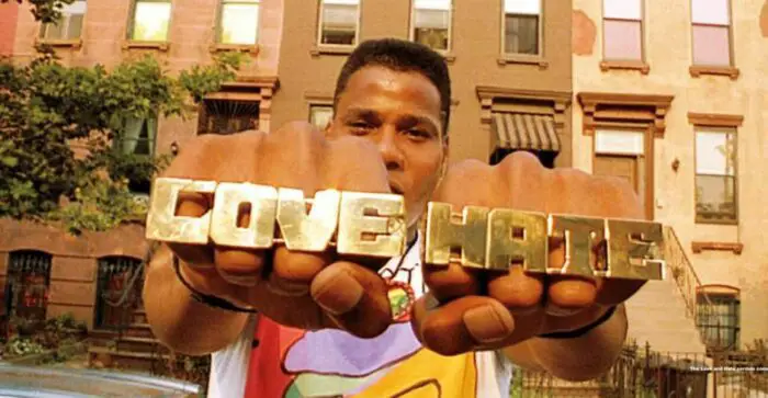 A man faces the camera wielding brass knuckles reading "Love" and "Hate"
