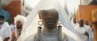 A woman wears a white hood in a funeral procession in Black Panther: Wakanda Forever