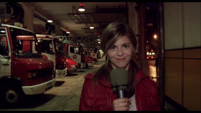Angela stands in a fire station, holding a microphone.