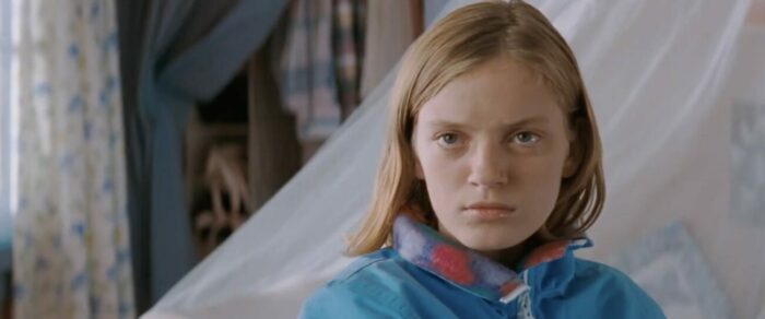 A close-up of Nicole (Sarah Polley) sitting in her bedroom, wearing a blue jacket.