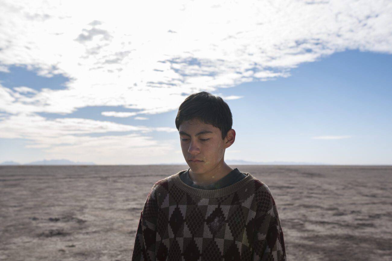 A young boy glances downward in front of an arid plain