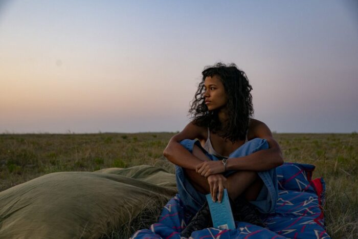 Taylor Russell as Maren on a hillside with her book, alone