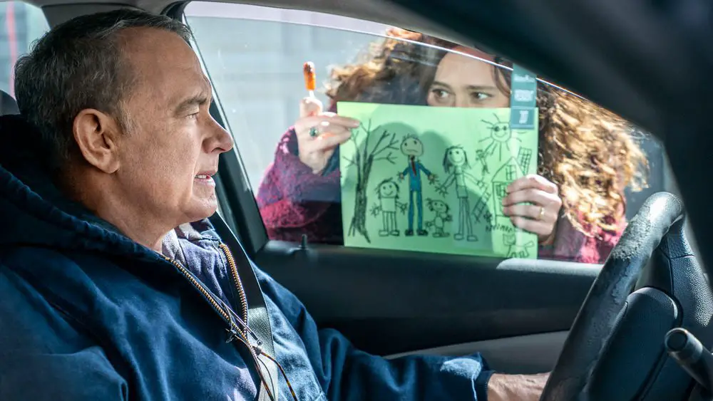A woman holds up a drawing to a car window for a man.