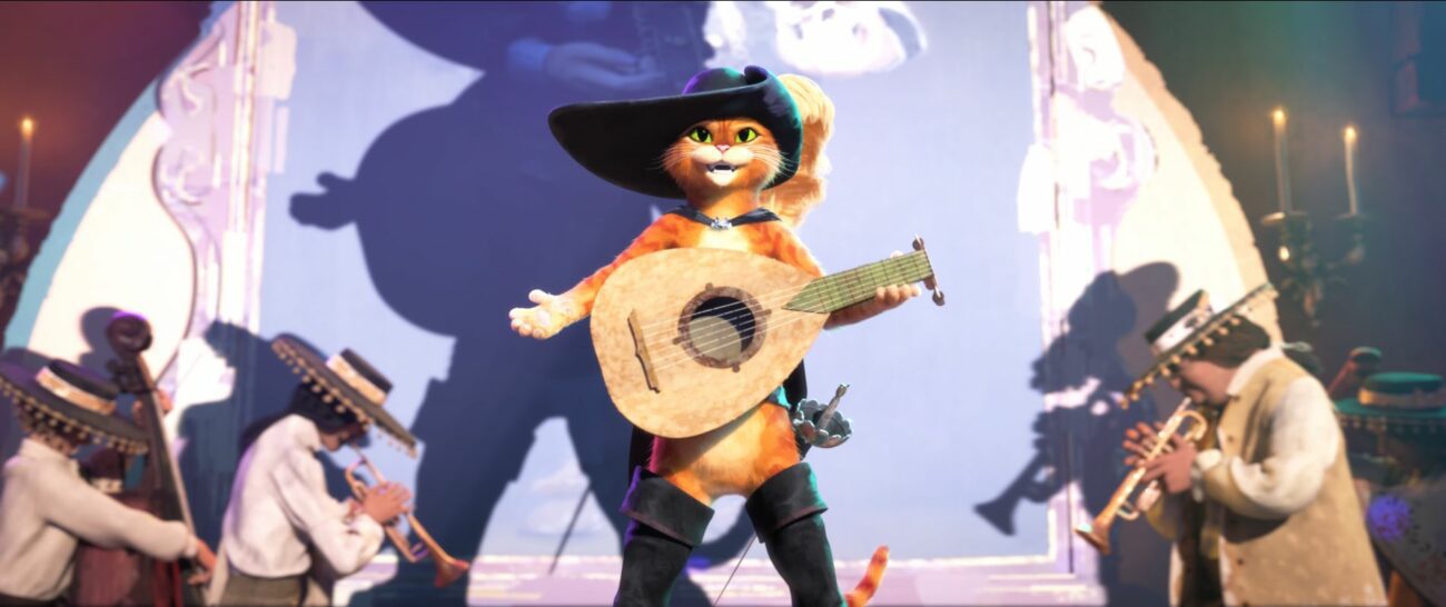 A cat is wearing a hat, boots, and guitar in front of a spotlight in Puss in Boots: The Last Wish