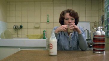 Delphine Seyrig sits in her kitchen and drinks from a glass in eanne Dielman, 23 Commerce Quay, 1080 Brussels