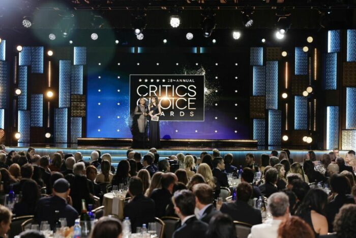 Two presenters stand on stage at the 28th Critics Choice Awards