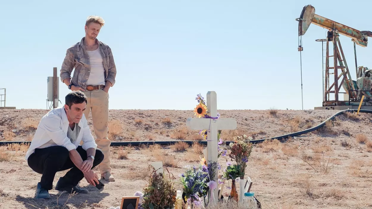 A scene from Vengeance with Ben and Ty paying respects to a cross next to an oil derrick.
