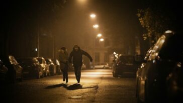 A man and a woman run through a city at night.