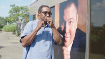 Muhammad Ali, Jr. pretends to box in front of a large photo of his father the boxer Muhammad Ali.