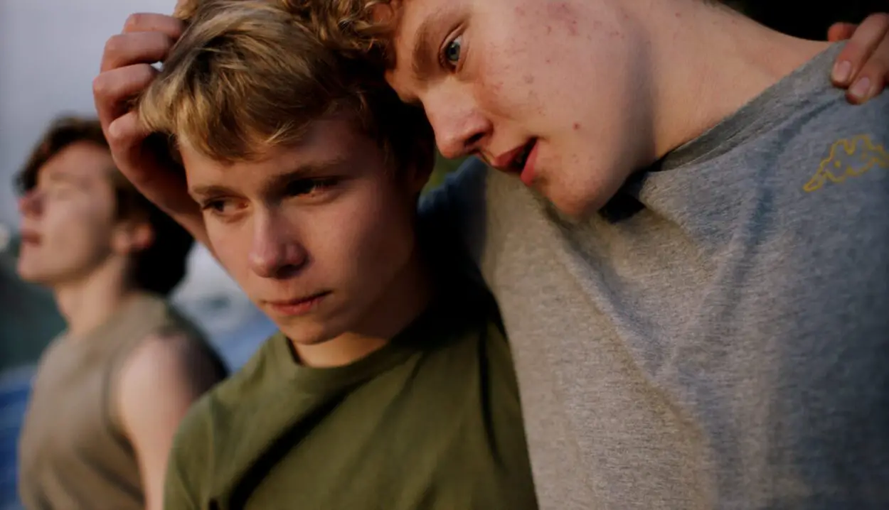 Three teen boys embrace on a rocky Icelandic shore.