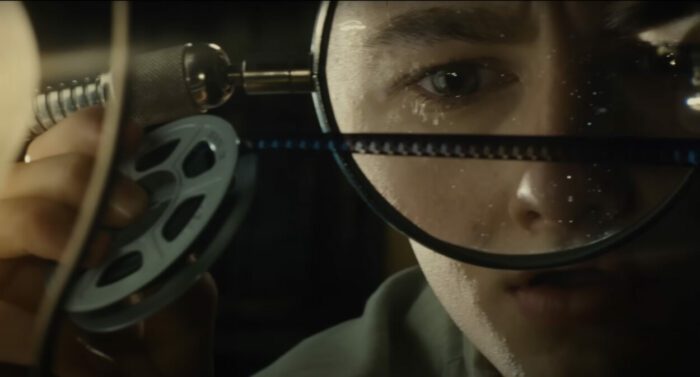 A young man looks at a strip of celluloid under a magnifying glass