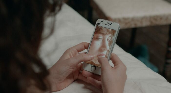 Avishrag (Elisheva Weil) examines her reflected image in her phone camera.