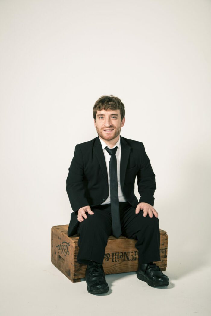 Nick Novicki sits on a wooden crate against a white background