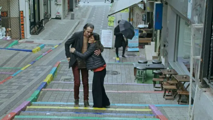 A man and a woman embrace on the street outside a cafe.