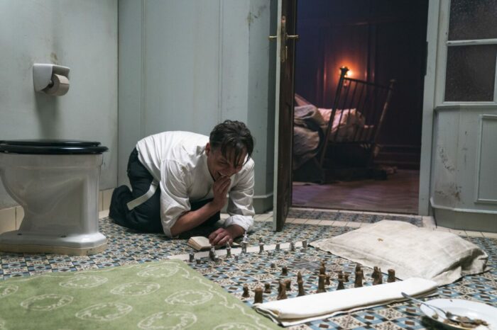 A man hovers over a makeshift chess game laid out on a grid of bathroom tiles.