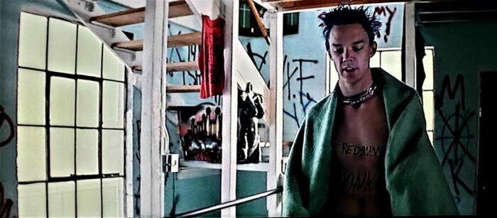 Matthew Lillard as Stevo walking around a graffiti covered apartment wearing only a towel and sporting spikey blue hair.