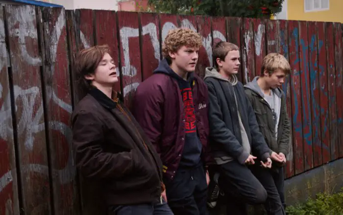 Four teen boys (Siggi, Konni, Balli, and Addi) stand in front of a graffiti-laden wall.
