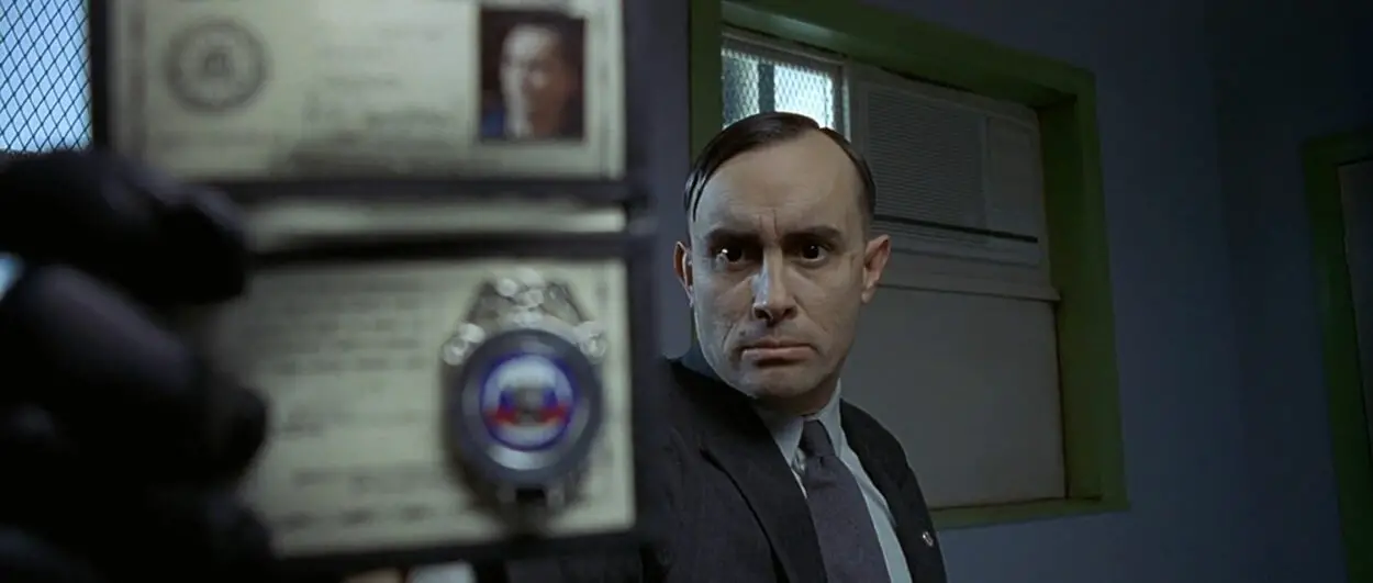Milton holds out his agency badge towards the camera.