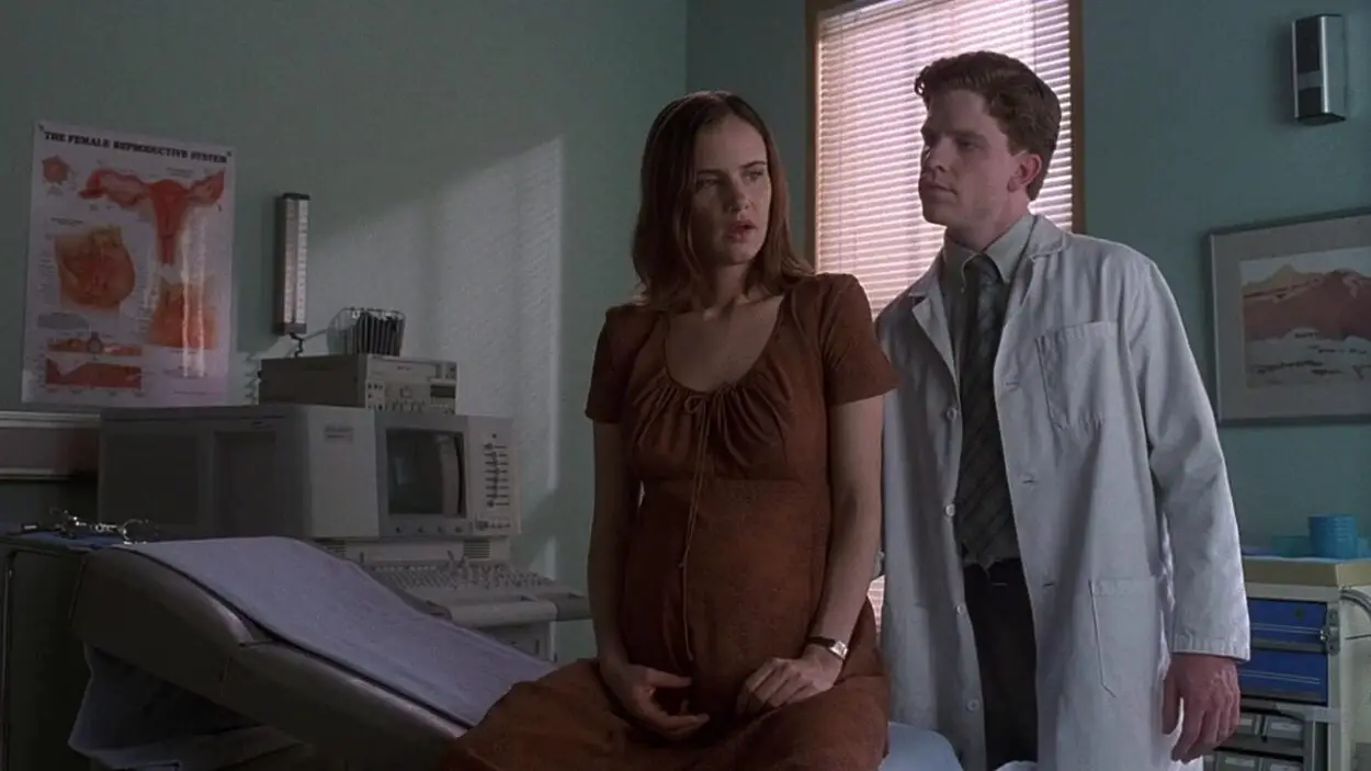 A visibly-pregnant Robin sits on a doctor's table with Painter next to her.