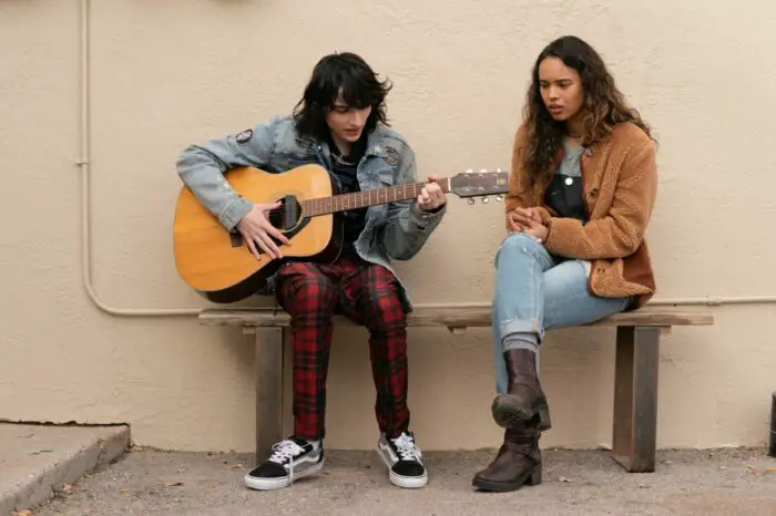 A teen boy plays a guitar for a girl on a bench in When You Finish Saving the World