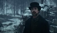 Christian Bale bearded and dressed in a top hat and style from the 1830s, alone in a snowy woods in the movie The Pale Blue Eye