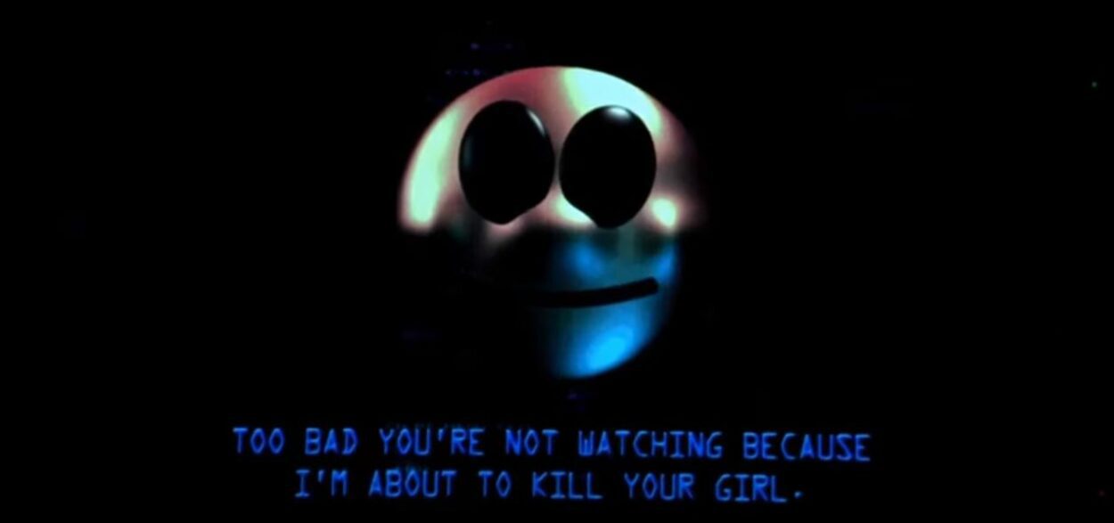 On a computer monitor, a smiling face with the text saying, "Too bad you're not watching because I'm about to kill your girl."