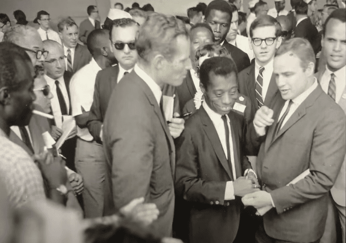 Heston with James Baldwin and Marlon Brando in a roomful of crowded onlookers, security agents, and reporters.