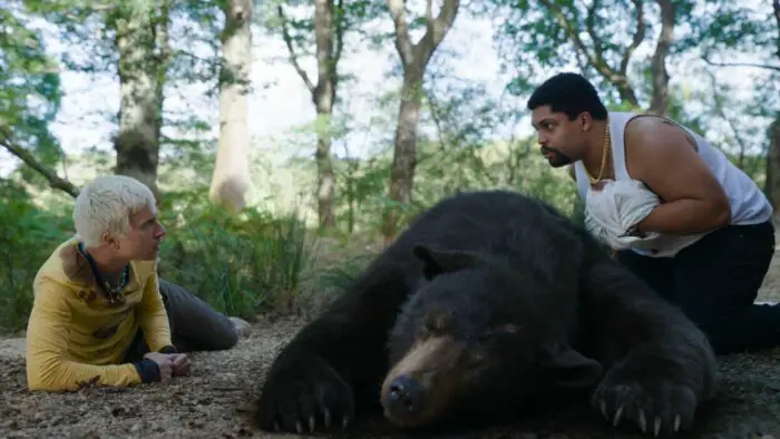 Two men look over a sleeping bear to each other in Cocaine Bear