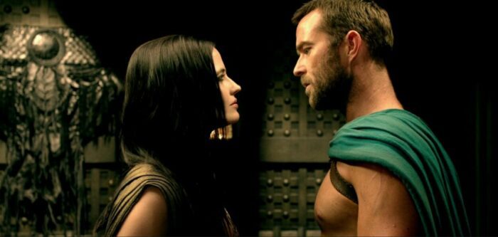 General Themistocles and Artemisia look at each other, with a wall that has ornate decorations in the background in 300: Rise of an Empire