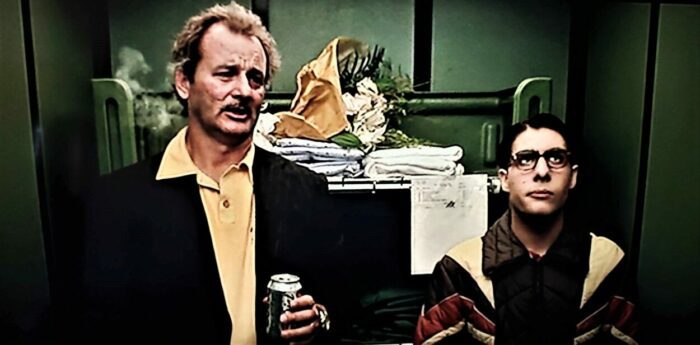 Bill Murray and Jason Schwartzman standing in elevator, Murray smoking and looking disheveled.