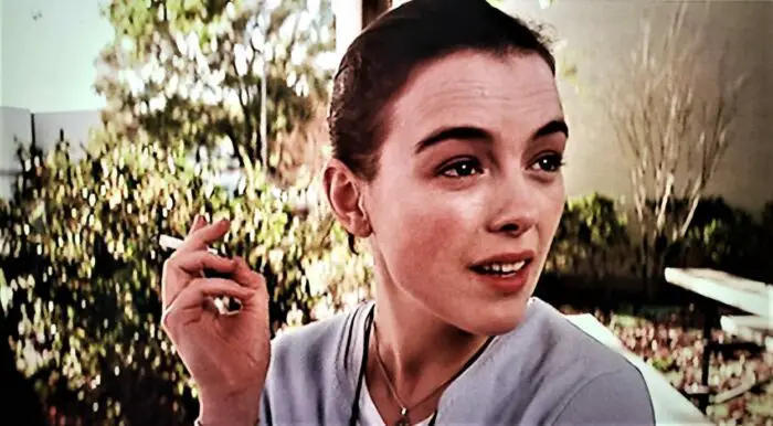 Olivia Williams sitting outdoors smoking on the bleachers in Rushmore