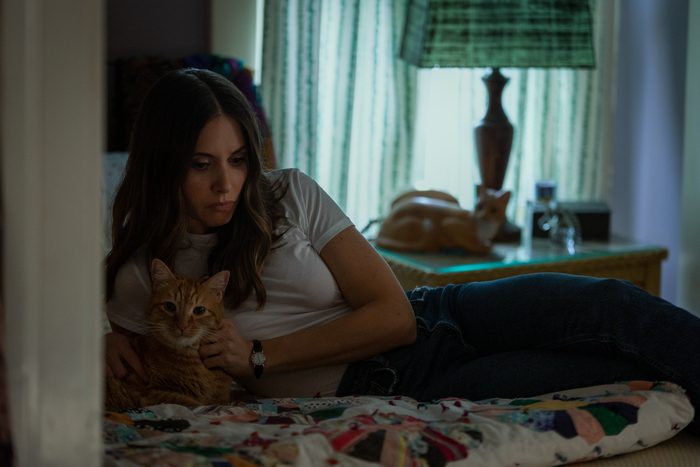 A woman reflects while laying on a bed with her cat.